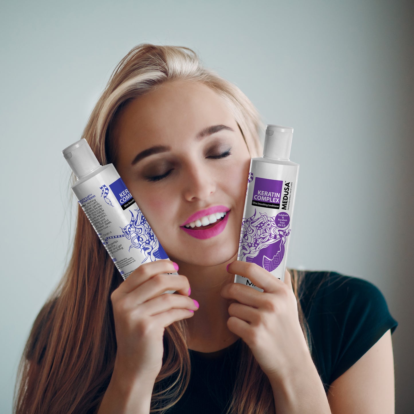 Smiling woman with beautiful, shiny hair, holding the Ultra Smoothing Shampoo and Conditioner to her face, eyes closed, enjoying the luxurious feel